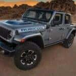 A silver 2024 Jeep Wrangler 4xe Rubicon is shown parked on a dirt path.