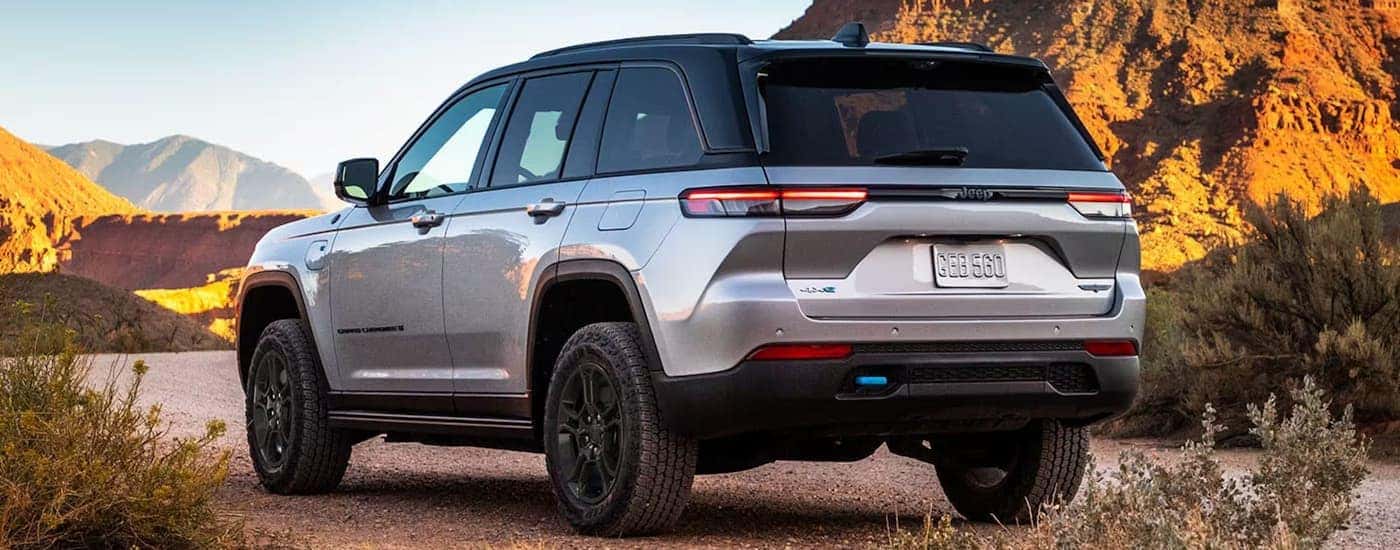 A silver 2024 Jeep Grand Cherokee 4xe is shown from a rear angle parked on a dirt road.