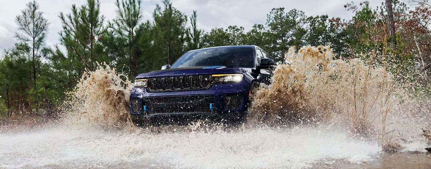 A blue 2024 Jeep Grand Cherokee is shown off-roading through a river.