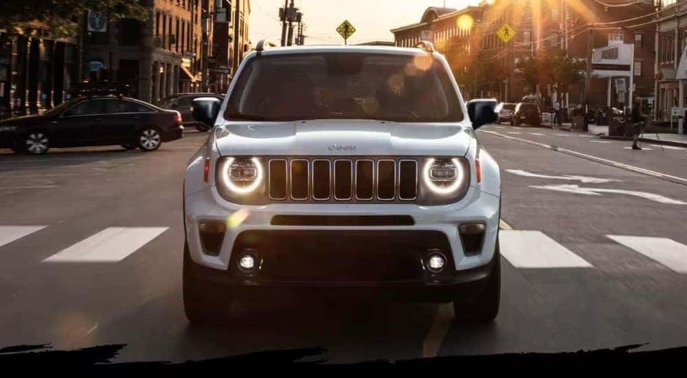 A white 2023 Jeep Renegade is shown driving on a crosswalk after visiting a Jeep dealer.