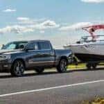 A black 2024 Ram 1500 is shown towing a boat after visiting a Ram dealer.