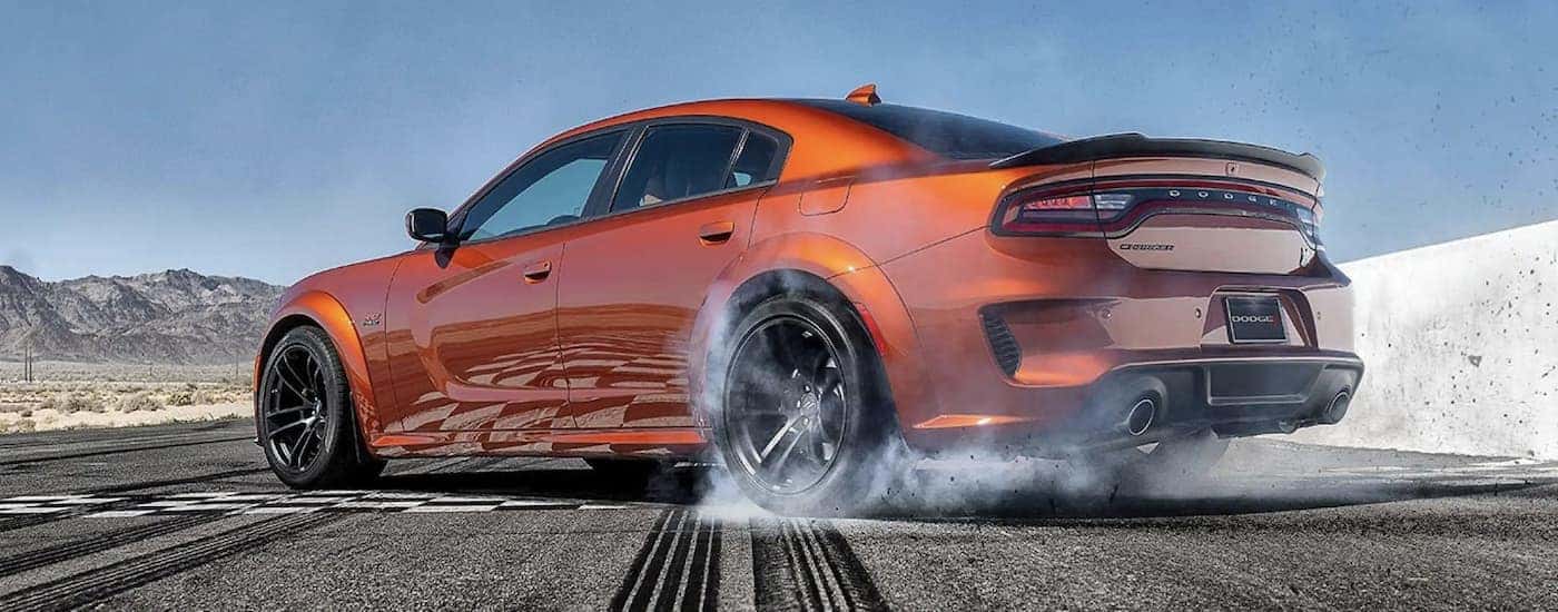 An orange 2022 Dodge Charger Scat Pack is shown performing a burnout.