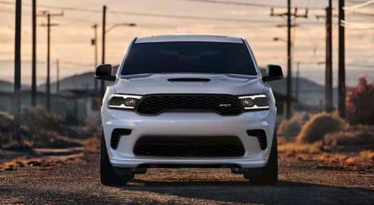 A white 2024 Dodge Durango SRT is shown driving on a dirt road after visiting a Dodge dealer.