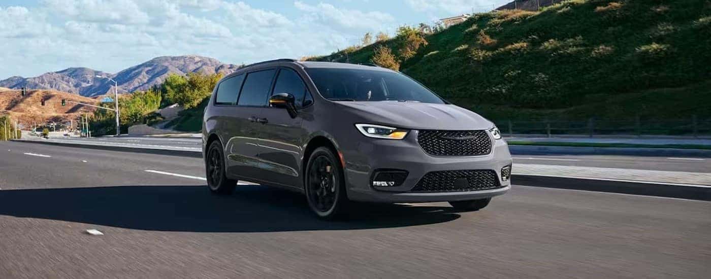 A grey 2024 Chrysler Pacifica is shown driving from a Chrysler dealer.