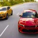 A yellow and a red 2024 Dodge Hornet are shown racing on a tree-lined road.