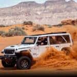 A white 2024 Jeep Wrangler Rubicon off-roading through sand dunes.