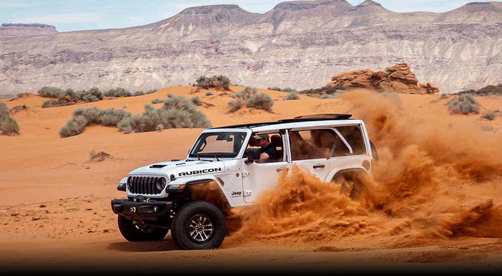 A white 2024 Jeep Wrangler Rubicon off-roading through sand dunes.