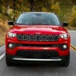 A red 2024 Jeep Compass is shown driving on a highway.
