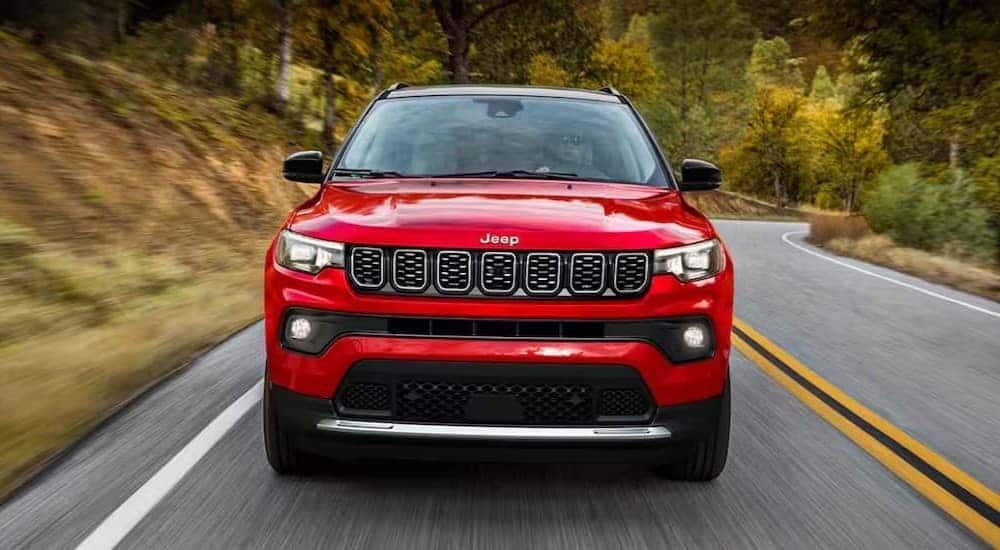 A red 2024 Jeep Compass is shown driving on a highway.