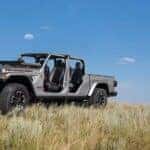A silver 2024 Jeep Gladiator Rubicon is shown parked on a field near two people.