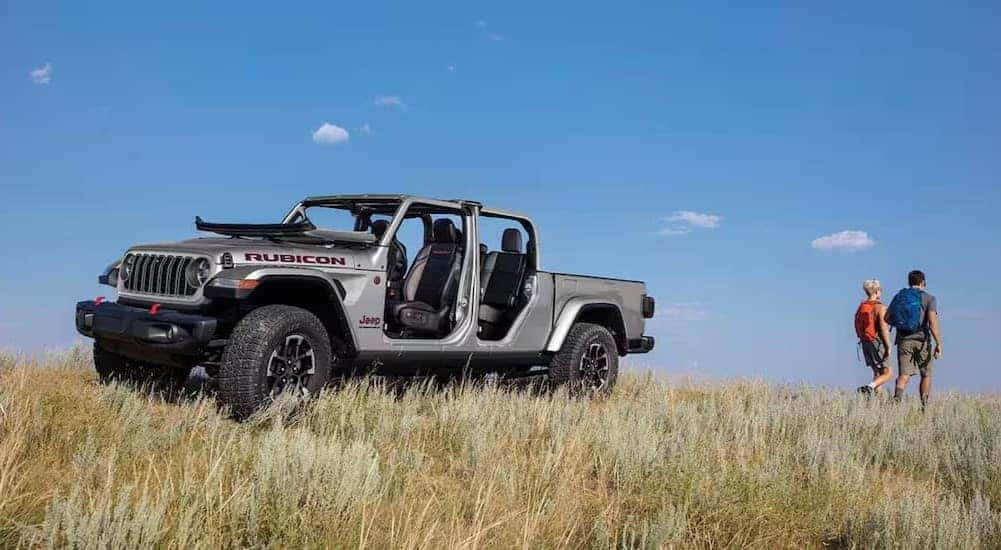 A silver 2024 Jeep Gladiator Rubicon is shown parked on a field near two people.