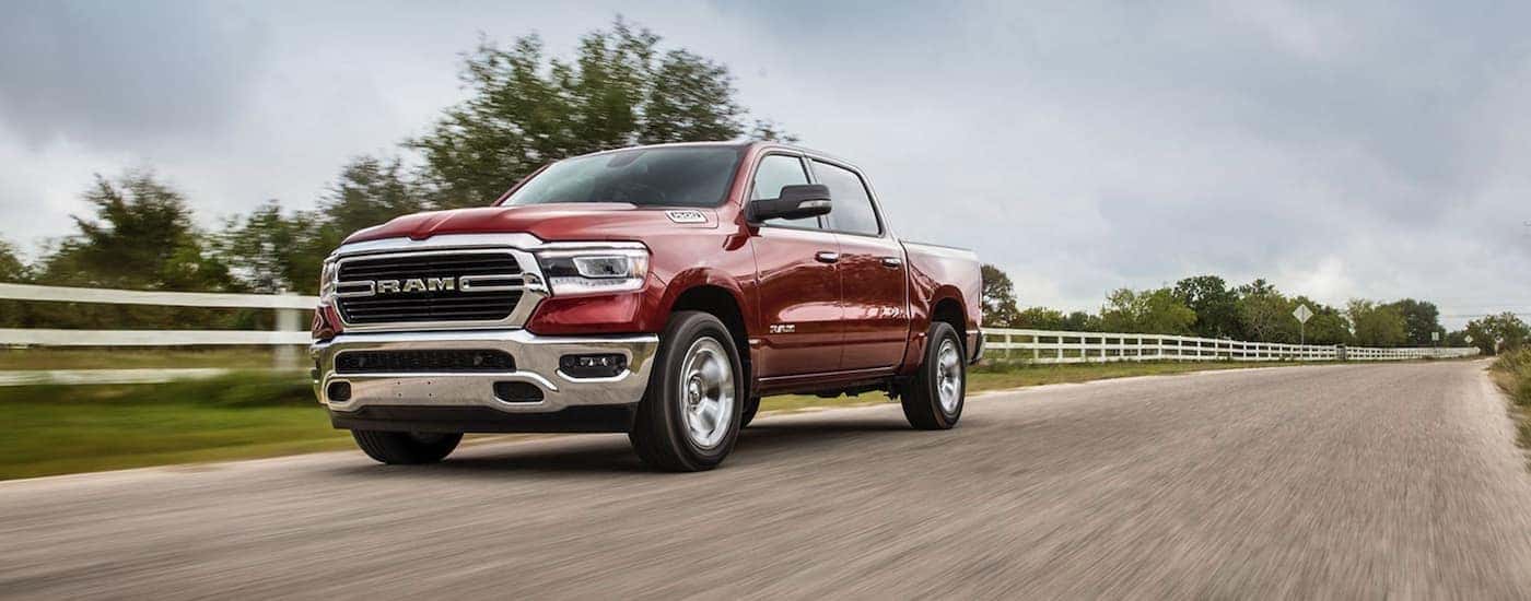 A red 2020 Ram 1500 Big Horn is shown driving near a long white fence.