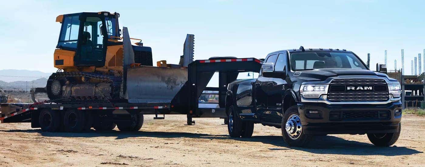 A black 2024 Ram 3500 is towing heavy machinery on a trailer at a construction site.