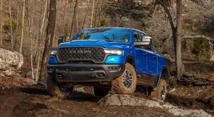 A blue 2025 Ram 1500 Rebel is off-roading on muddy trail.