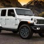 A white 2025 Jeep Wrangler Unlimited is shown parked on a gravel lot.
