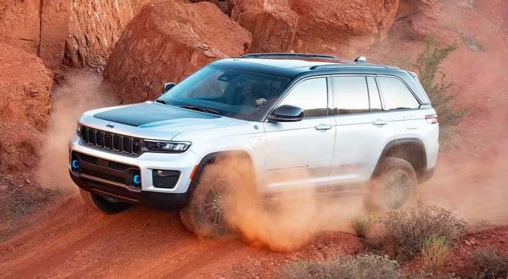 A white 2025 Jeep Grand Cherokee 4xe is shown driving off-road.