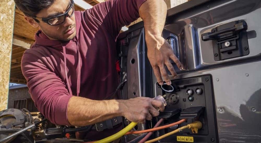 A person is shown using an electrical outlet on a 2022 Ford F-150 Lightning after viewing used trucks for sale in Florence.