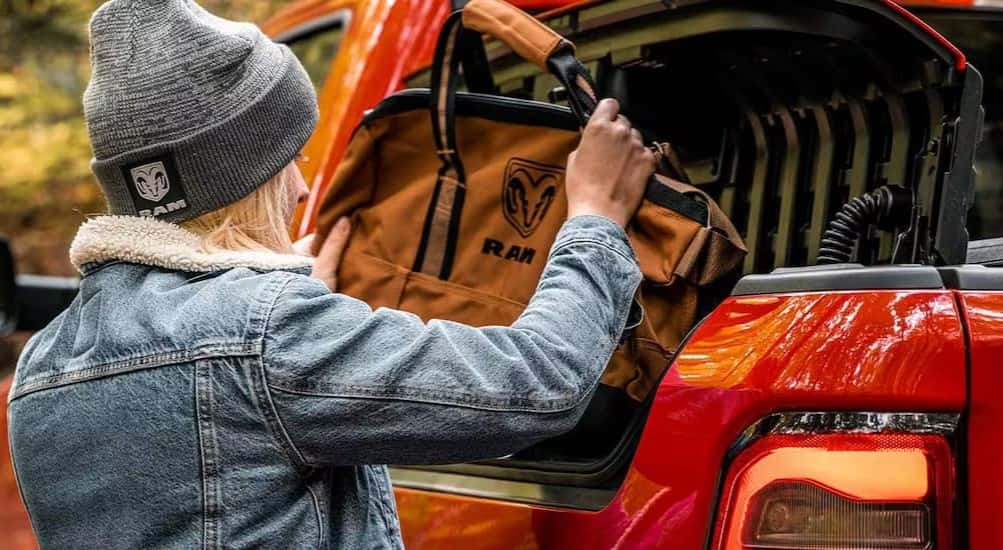 A person is shown placing a bag into the Rambox cargo management system in a red 2024 Ram 1500.