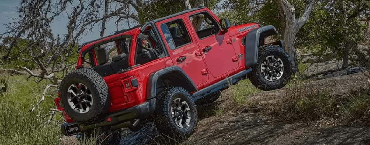 A red 2025 Jeep Wrangler Rubicon off-roading on a path through a forest.