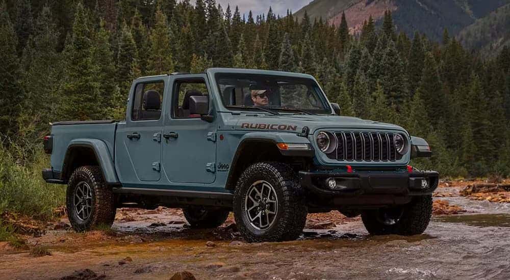 A blue 2025 Jeep Gladiator Rubicon is off-roading through a stream.