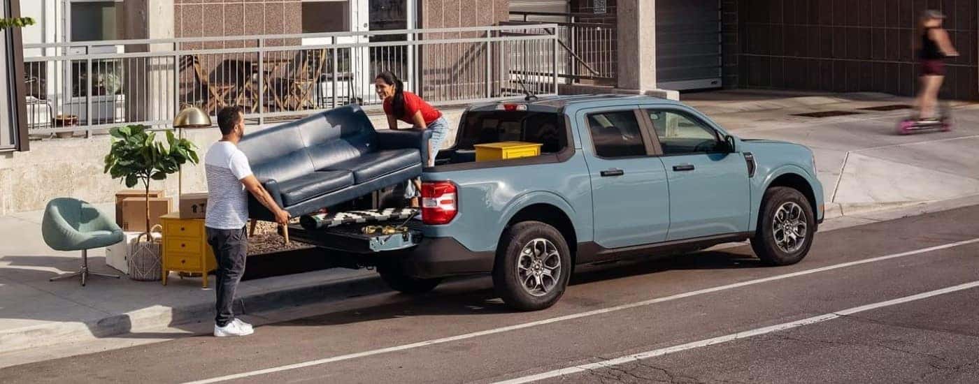 Rear view of people loading a couch into the bed of a blue 2022 Ford Maverick.