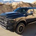 A black 2025 Ram 2500 is shown driving on a highway.