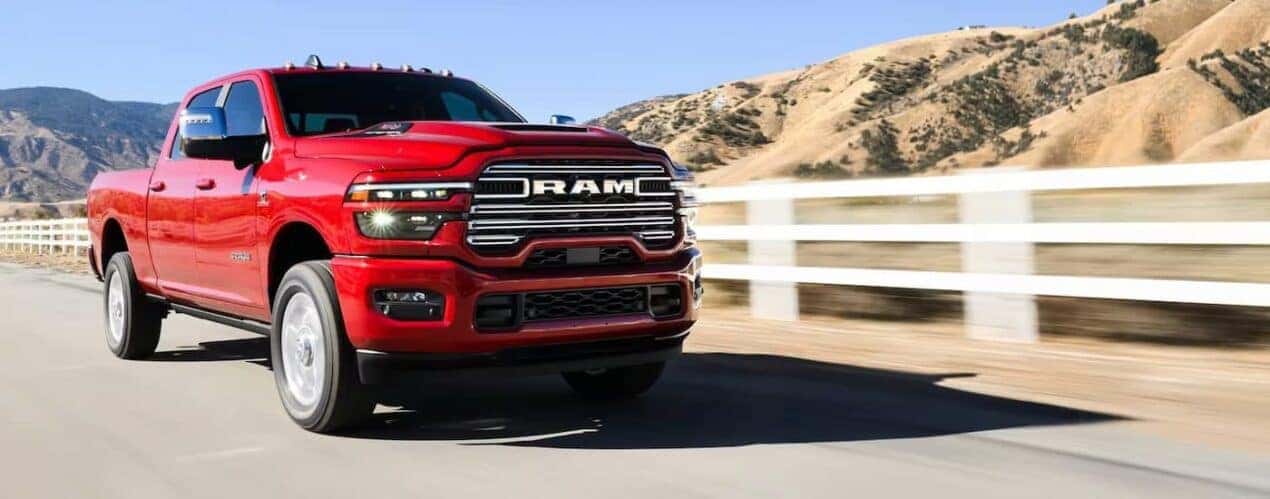 A red 2025 Ram 2500 is shown driving near a white fence.