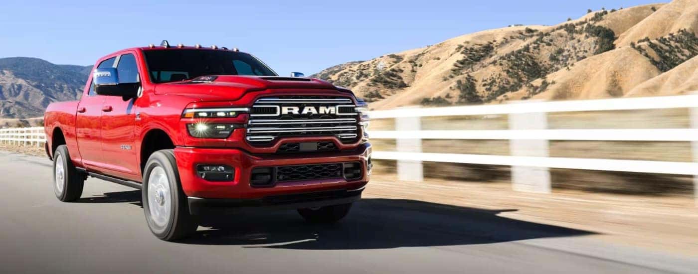 A red 2025 Ram 2500 is driving past a white fence.