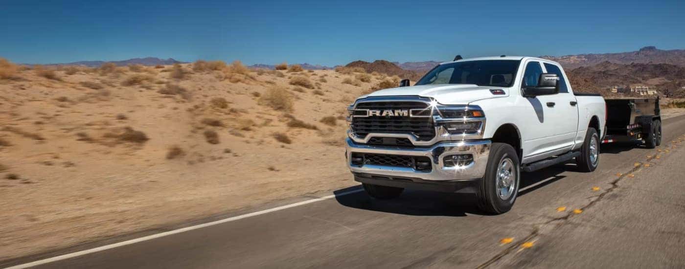 A white 2025 Ram 2500 is towing a trailer on a highway.