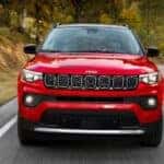 A red 2025 Jeep Compass driving on a highway.