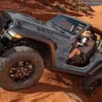 A gray 2025 Jeep Wrangler Willys off-roading on a dirt path.