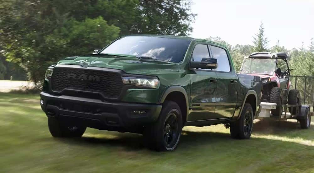 A green 2026 Ram 1500 Rebel towing a trailer on grass.