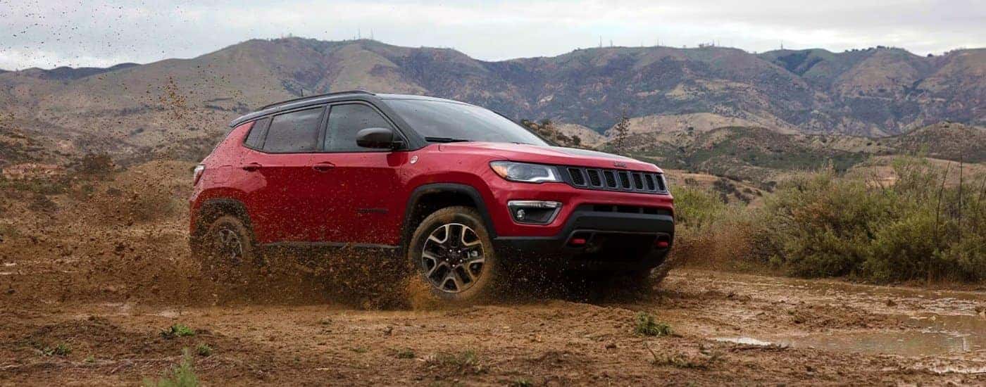 A red 2021 Jeep Compass Trailhawk is off-roading in mud in front of mountains.