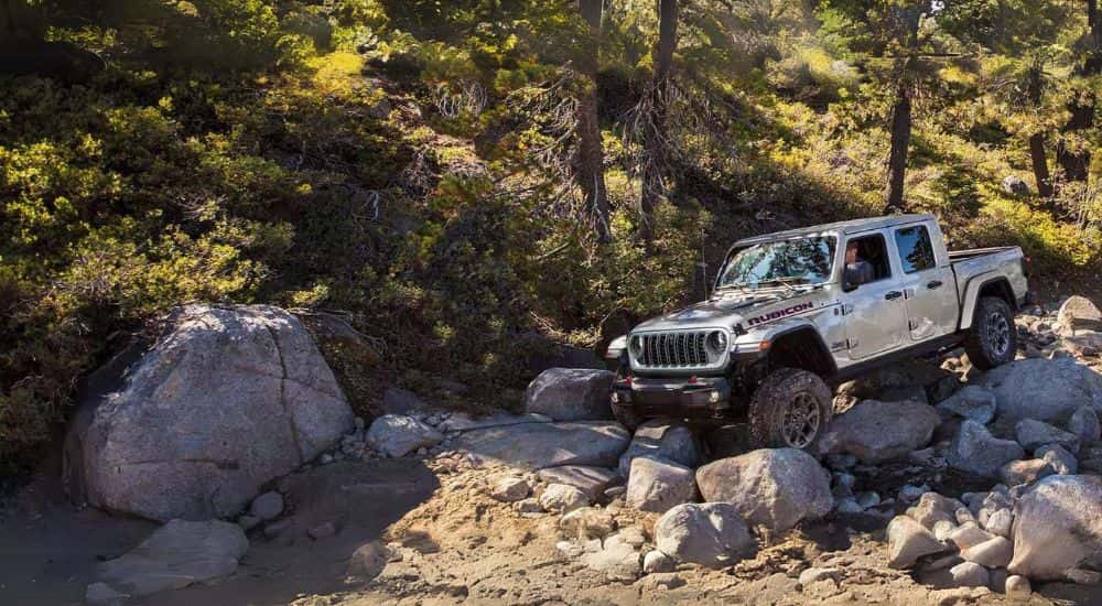A silver 2024 Jeff Gladiator Rubicon off-roading on rocks