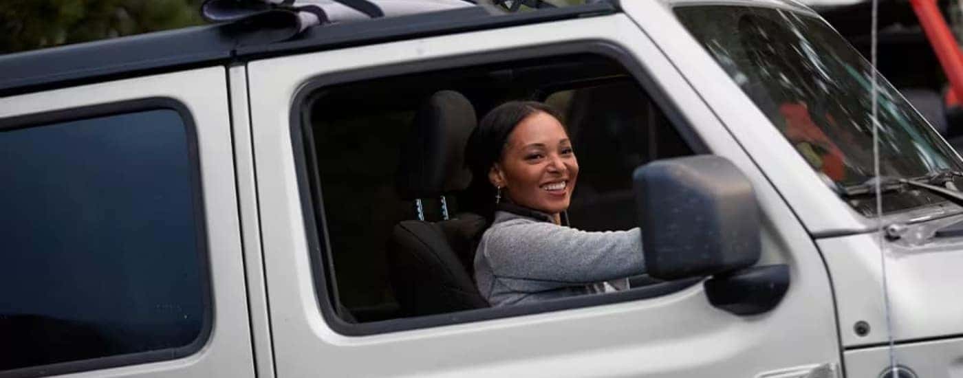 A smiling person driving a white 2023 Jeep Gladiator.
