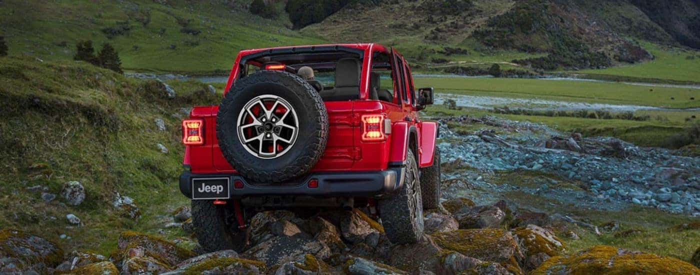 Rear of a red 2024 Jeep Wrangler Unlimited driving off-road.