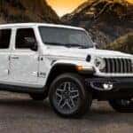 White 2025 Jeep Wrangler from the front at an angle parked in the mountains.