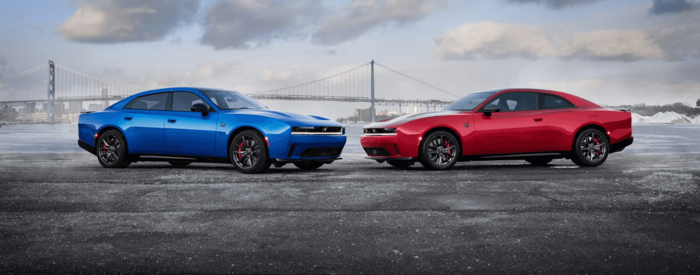 A red and a blue 2026 Dodge Charger parked in front of a bridge