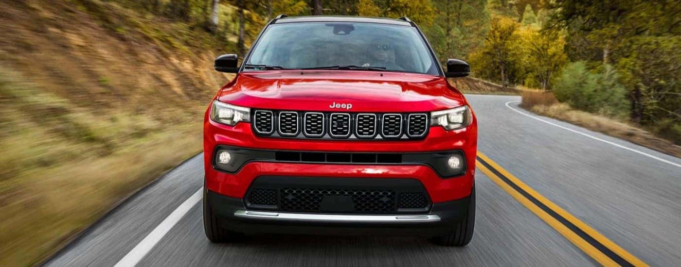 A red 2024 Jeep Compass driving down a rural road