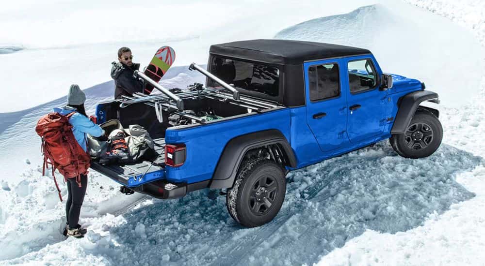 Blue 2026 Jeep Gladiator Sport edition parked on snow with a couple removing winter sports equipment