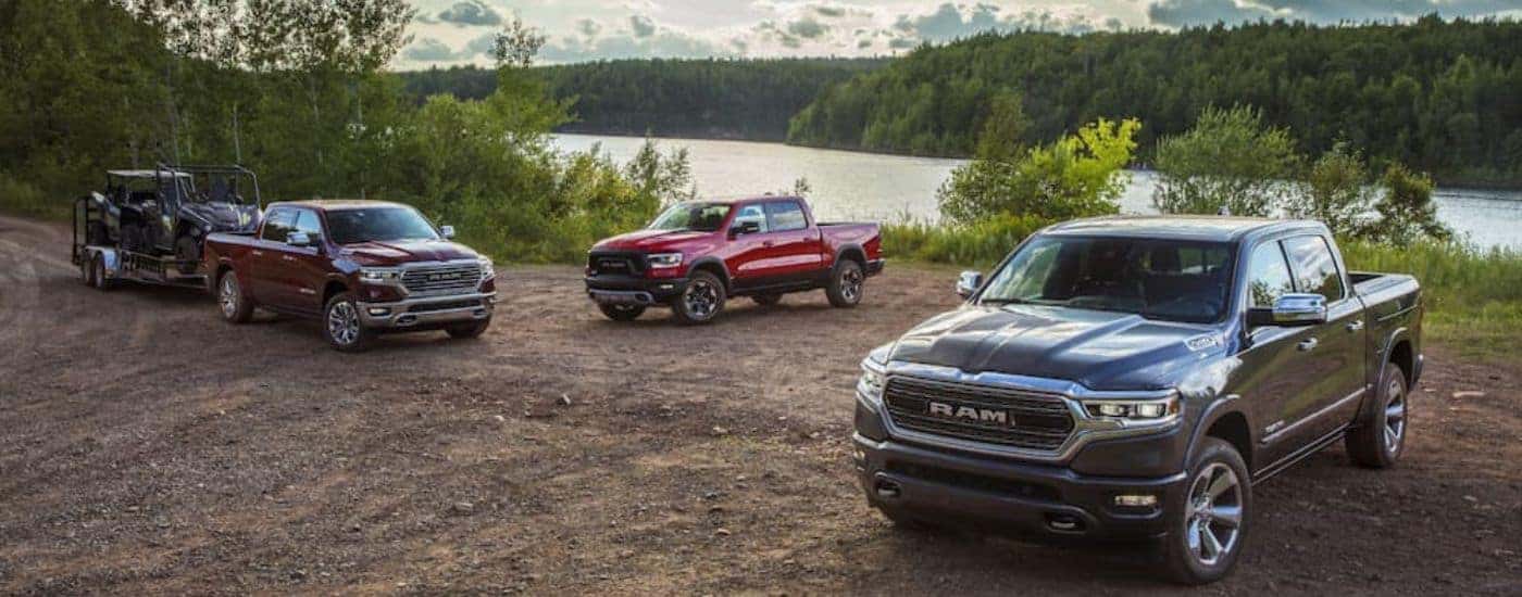 Three 2020 Ram 1500 trucks are parked on a dirt patch in front of a lake