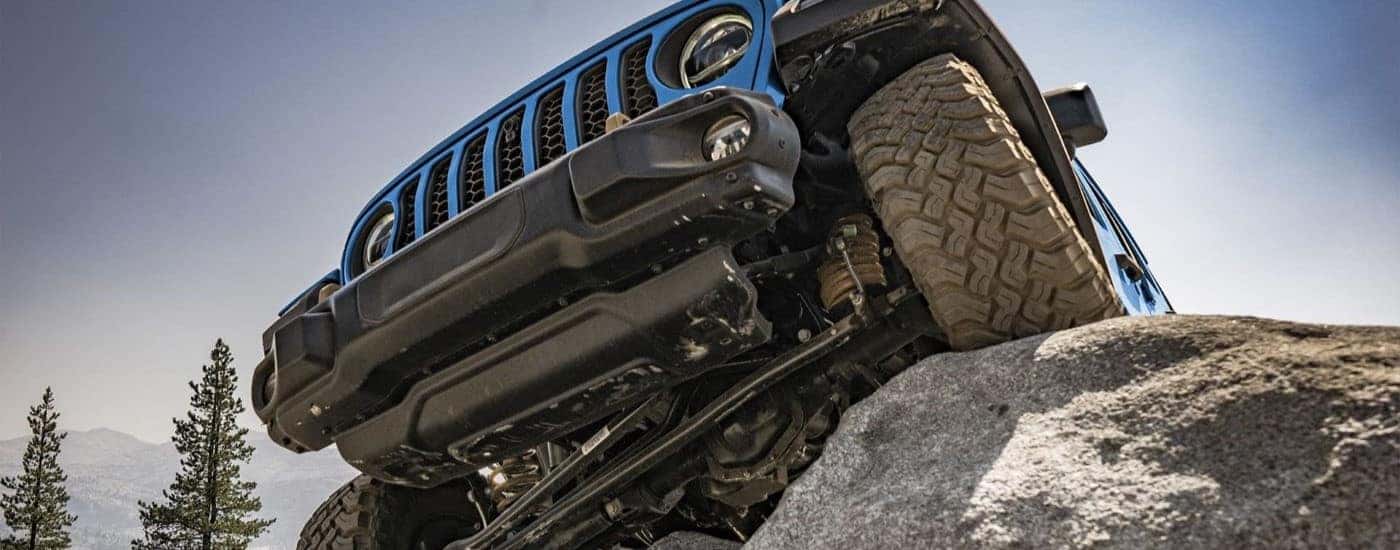 Blue 2022 Jeep Wrangler is shown driving over a large rock
