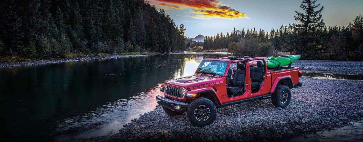 A red 2024 Jeep Gladiator parked next to a lake with a kayak.
