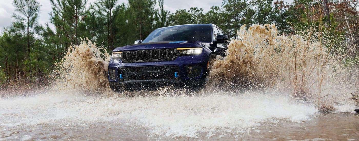 A blue 2024 Jeep Grand Cherokee is driving through a river.