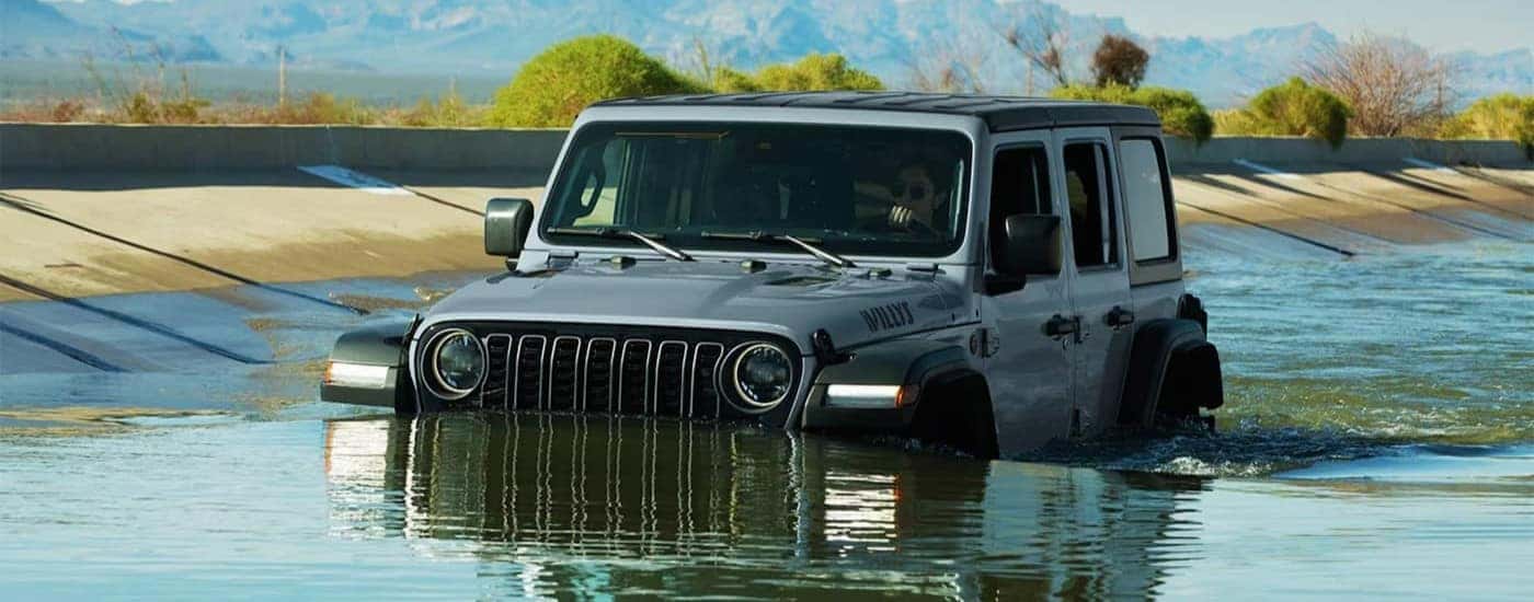 A gray 2026 Jeep Wrangler Willys driving in water.