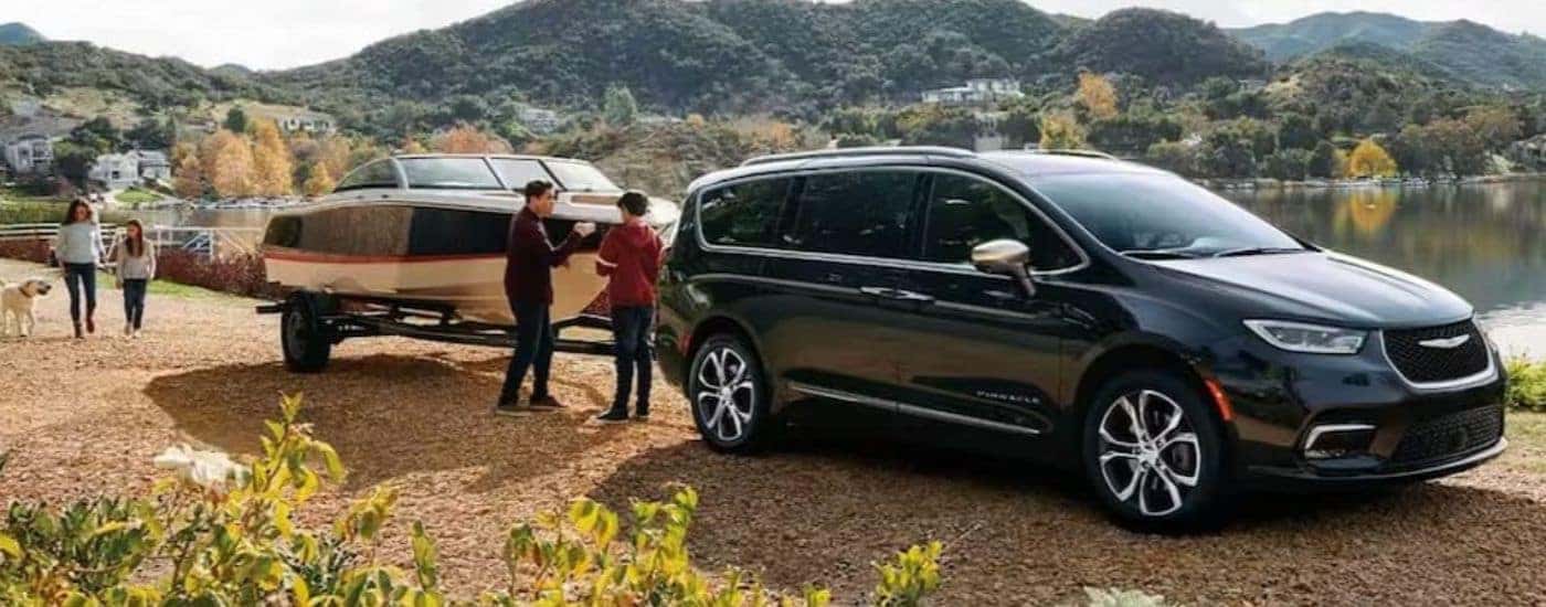A black 2023 Chrysler Pacifica is shown towing a boat near a lake.