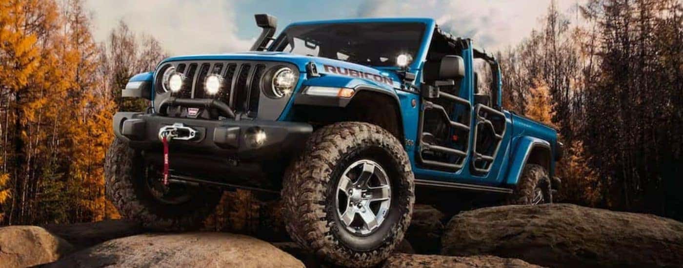 A blue 2021 Jeep Gladiator with no roof and doors is parked on rocks.