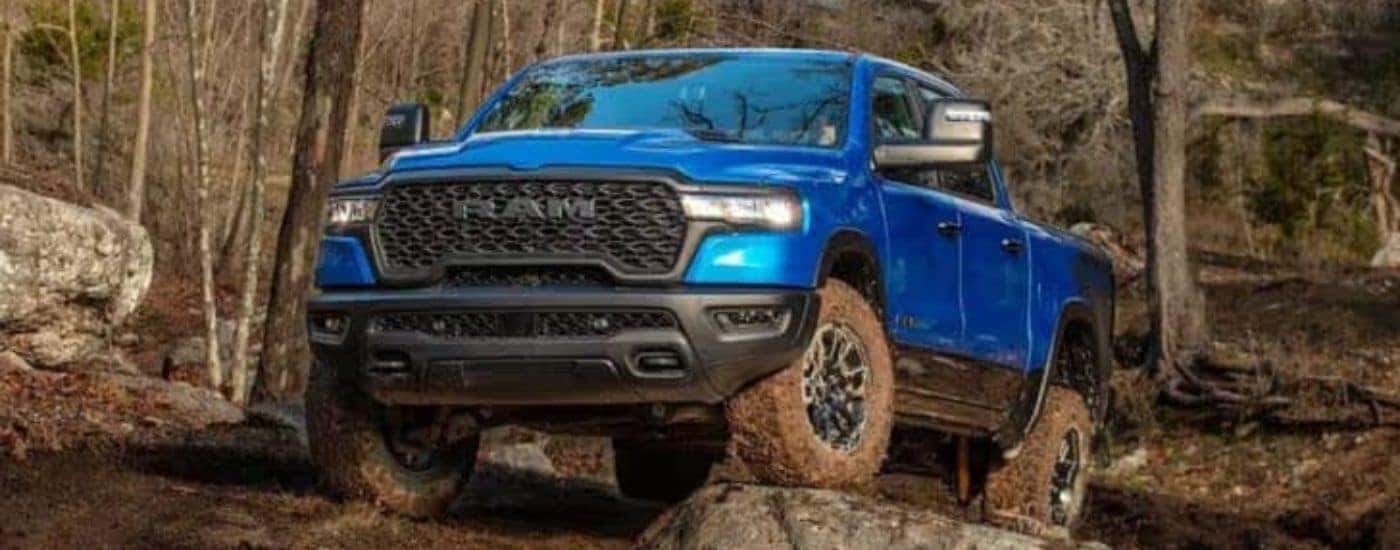 A blue 2025 Ram 1500 Rebel is off-roading on muddy trail.