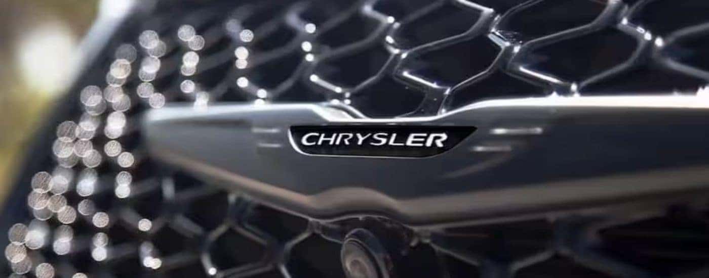 A close-up of the Chrysler badge is shown on a 2025 Chrysler Pacifica.