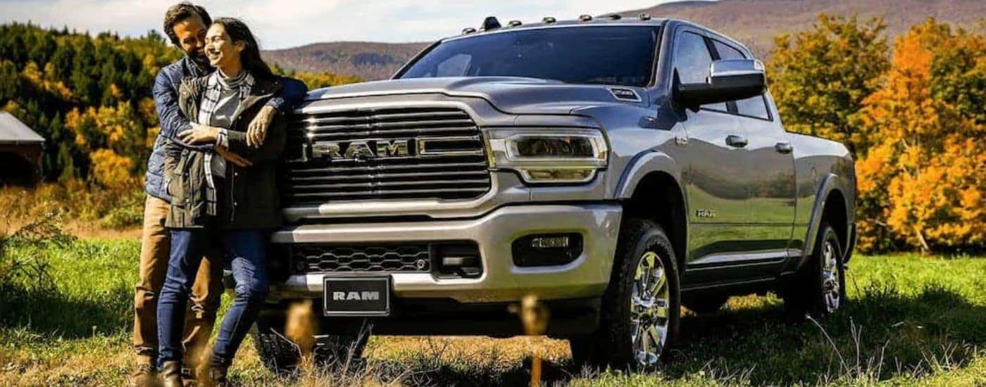 A couple is shown standing in front of a silver 2022 Ram 2500 parked in an open field.